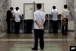 A man reads the local newspaper displayed on a stand while others browse the intranet system on computers at the Grand People's Study House Monday, July 24, 2017, in Pyongyang, North Korea.