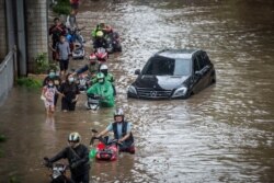 Warga mendorong sepeda motornya melewati air di daerah terdampak banjir menyusul hujan deras di Jakarta, 20 Februari 2021. (Foto: Antara/Aprillio Akbar via REUTERS)