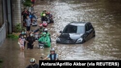 Warga mendorong sepeda motornya melewati air di daerah terdampak banjir menyusul hujan deras di Jakarta, 20 Februari 2021. (Foto: Antara/Aprillio Akbar via REUTERS)