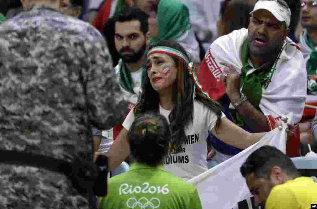 Darya Safai pleads with security personnel as they consider removing her for holding up a large sign protesting the fact that women have not been allowed to attend volleyball matches in Iran, during a men's preliminary volleyball match between Egypt and I