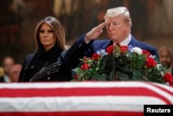 US President Donald J. Trump, with First Lady Melania Trump, salutes the casket containing the body of former US President George H.W. Bush in the Rotunda of the US Capitol in Washington, DC, December 3, 2018.