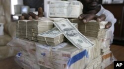 FILE: An unidentified man displays the equivalent of $100 United States on a scale in Harare, Wednesday, March, 5, 2008. The Zimbabwean currency tumbled to a record $25 million for a single US dollar.