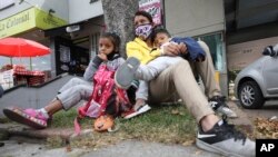 Venezuelan migrant Katerine Valero, 29, and her children Dariusca, 8, left, and Wilkerson, 4, rest outside a strip mall in Bogota, Colombia, Feb. 9, 2021.
