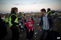 A volunteer, left, hands water and food to a Syrian refugee woman carrying a baby after she crossed the border between Serbia and Hungary in Roszke, southern Hungary, Sept. 14, 2015.