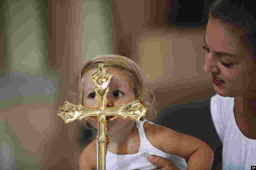 Anarita Mihilli is being held by her mother as she kisses the gold plated cross in the church of the Black Madonna, during the feast of Assumption in the village of Letnica, Kosovo.