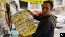 An Afghan store clerk shows a calendar with pictures of Afghan leaders including Mullah Mohammad Omar, bottom row, second left, in Kandahar, south of Kabul, Afghanistan, July 30, 2015. 