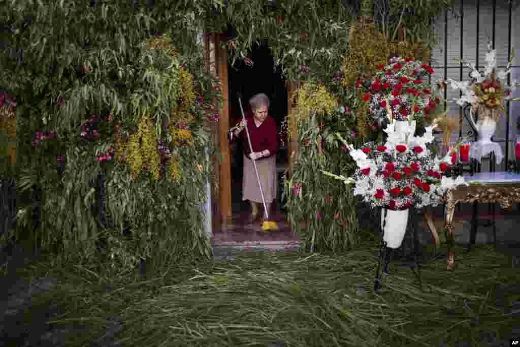 A woman cleans the floor of her house decorated with flowers and branches as she waits for a Corpus Christi procession in Zahara de la Sierra village, in Cadiz province, Spain.