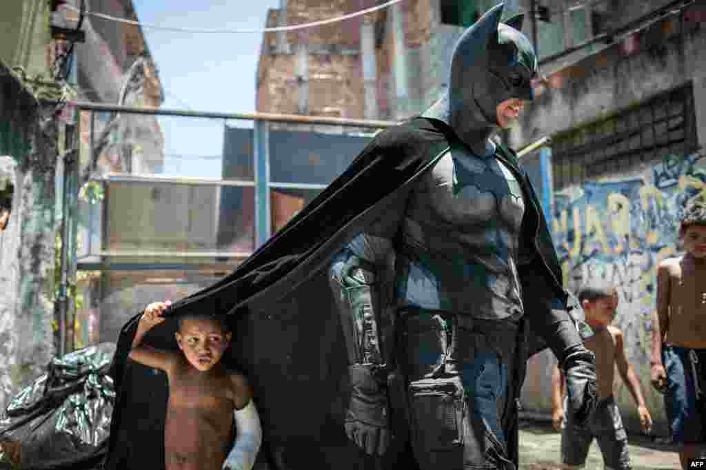 Trẻ em chơi quanh một người trong bộ trang phục Batman ở khu ổ chuột Favela do Metro, khu vực ngay gần sân vận động Maracana ở thành phố Rio de Janeiro, Brazil. Những hộ gia đình sống trong khu nhà ổ chuột gần sân vận động này không cho phá bỏ nhà của họ trong một dự án tân trang khu vực trước Giải bóng đá World Cup vào tháng 6.