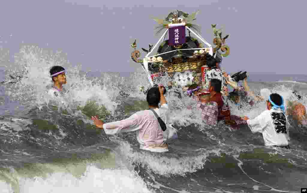 Participants cheer on a portable shrine carried by others as they parade through the sea during a purification rite at the annual Hamaori Festival at Southern beach in Chigasaki, west of Tokyo.