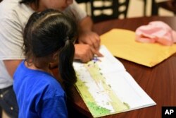 FILE - In this photo provided by U.S. Immigration and Customs Enforcement, a child looks at a book at South Texas Family Residential Center in Dilley, Texas, Aug. 9, 2018.