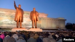 North Koreans bow to bronze statues of North Korea's late founder, Kim Il Sung, left, and late leader, Kim Jong Il, at Mansudae in Pyongyang in this picture provided by Kyodo, Dec. 16, 2014.