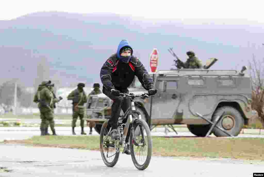 A man rides a bicycle as armed men, believed to be Russian serviceman, stand guard outside a Ukrainian military unit in the village of Perevalnoye, near Simferopol, Crimea, Ukraine, March 11, 2014. 