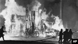 FILE - Firefighters try to control blazing buildings after riots in Detroit, July 25, 1967. Hundreds of fires were reported in the city. 