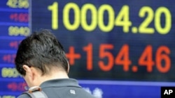 A man checks his mobile phone in front of an electric quotation board flashing the closing rate of the Tokyo Stock Exchange market in Tokyo on May 2, 2011