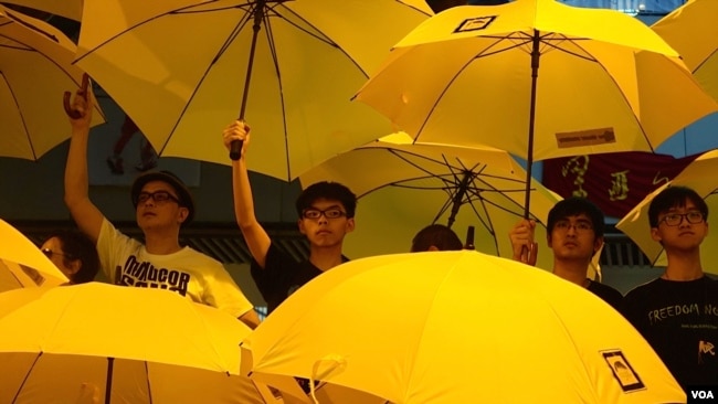资料照：黄之锋和周永康与其他“雨伞运动”领袖一起在集会上撑开黄色雨伞。一个月前，警方向争取民主的抗议人群发射催泪弹。（2014年10月28日）