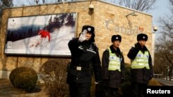A police officer gestures at the photographer as security staff stand guard outside the Canadian embassy in Beijing, Dec. 20, 2018. 