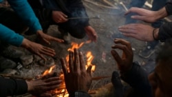 Bracing against harsh winter weather inside an abandoned hangar migrants warm their hands while gathered near the Hungarian border, outside of the village of Majdan, Serbia, Jan. 11, 2022.