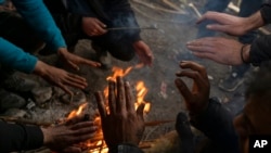 Inside an abandoned hangar migrants warm their hands as they gather outside the village of Mazdan, Serbia, January 11, 2022, near the Hungarian border against harsh winter weather.