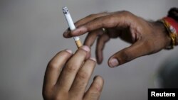 FILE - A man passes a cigarette to another as they sit on a pavement along a road in New Delhi, India, Aug. 18, 2015. 