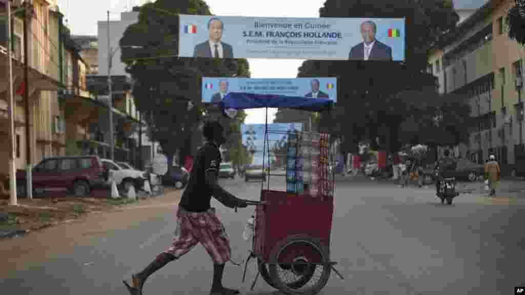 Un vendeur de rue guinéen pousse son chariot sous des banderoles mettant en vedette le président français François Hollande et son homologue guinéen Alpha Condé à Conakry, en Guinée, mercredi 26 novembre 2014.