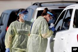 Healthcare workers conducts COVID-19 tests at a drive-thru coronavirus testing site, Tuesday, April 21, 2020, in Sanford, Fla. (AP Photo/John Raoux)