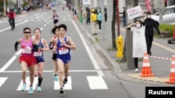 A spectator raises a paper sign reading 'It is impossible to hold the Olympics, face up to reality' along the race route during the half-marathon as part of Hokkaido-Sapporo Marathon Festival 2021.