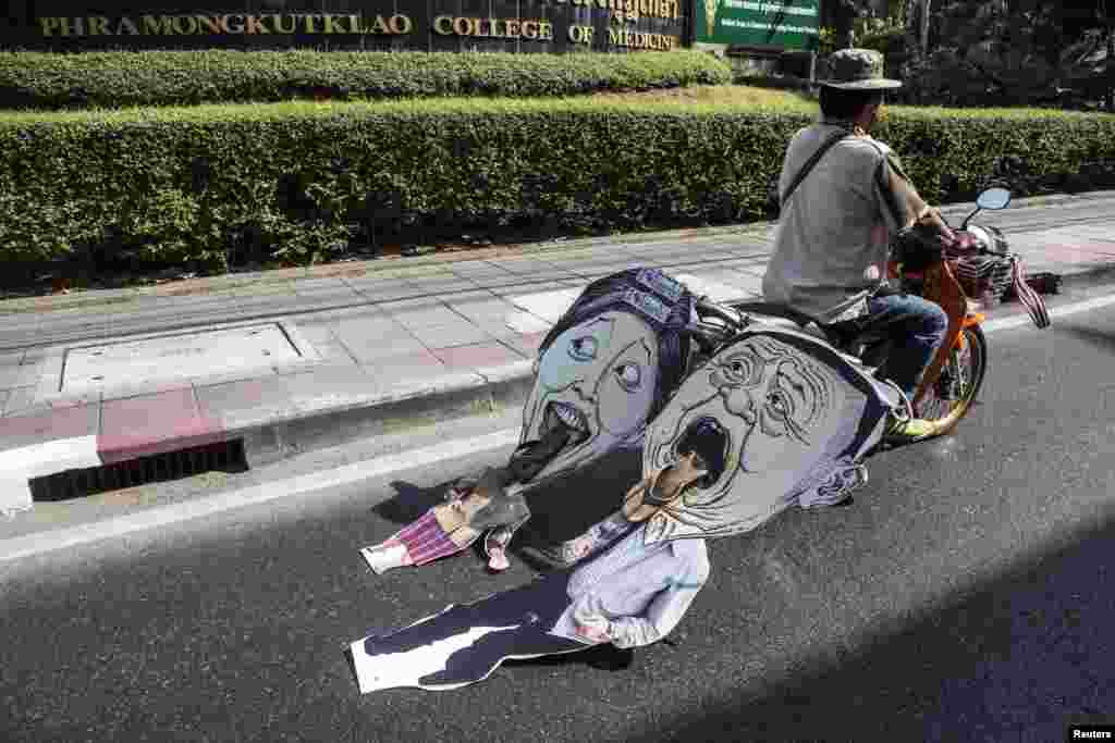 An anti-government protester pulls a caricature of Thailand&#39;s Prime Minister Yingluck Shinawatra and her brother Thaksin as he rides during a rally in central Bangkok.