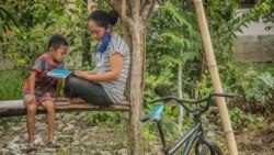 Seorang ibu dan anak yang sedang membaca booklet informasi Virus Corona di Desa Kilo, Kecamatan Poso Pesisir, Kabupaten Poso, Sulawesi Tengah, 30 Maret 2020. (Foto: Institut Mosintuwu)