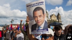 A man holds up a campaign poster of Guatemala's President Jimmy Morales during a gathering to show support for the Commissioner of the United Nations International Commission Against Impunity, Ivan Velasquez in Guatemala City, Saturday, Aug. 26, 2017. 