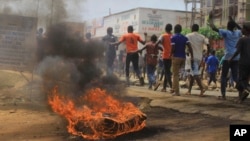 Protesters walk past a burning tyre in the Eastern Congolese town of Beni, Friday Dec. 28, 2018, as they demonstrate against the election postponed until March 2019, announced by Congo's electoral commission for Beni residents that is blamed on a deadly Ebola outbreak. 