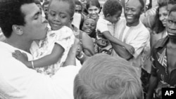 Mohamed Ali plante une bise sur la joue d’une jeune admiratrice zaïroise venue l’applaudir, avec d’autres supporters, à son camp d'entraînement N’Sele au Zaïre, 26 octobre 1974. (AP Photo)