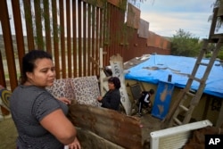 Yuli Arias, posa cerca de una parte renovada del muro fronterizo, mientras su madre Esther Arias está de pie frente a la casa de la familia que una vez fue amenazada por la construcción a lo largo de la frontera en Tijuana, México.
