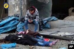 This photo provided by the Syrian Civil Defense White Helmets, which has been authenticated based on its contents and other AP reporting, shows a Syrian boy sitting next to bodies after artillery fire struck the Jub al-Quba district in Aleppo, Nov. 30m, 2016.