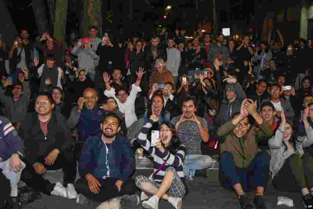 People react as they watch the film "Roma," by Mexican Director Alfonso Cuaron, win the Oscar for best foreign language film at the 91st Academy Awards, shown on a screen installed for a watch party in a plaza in the Roma neighborhood of Mexico City, Feb. 24, 2019.