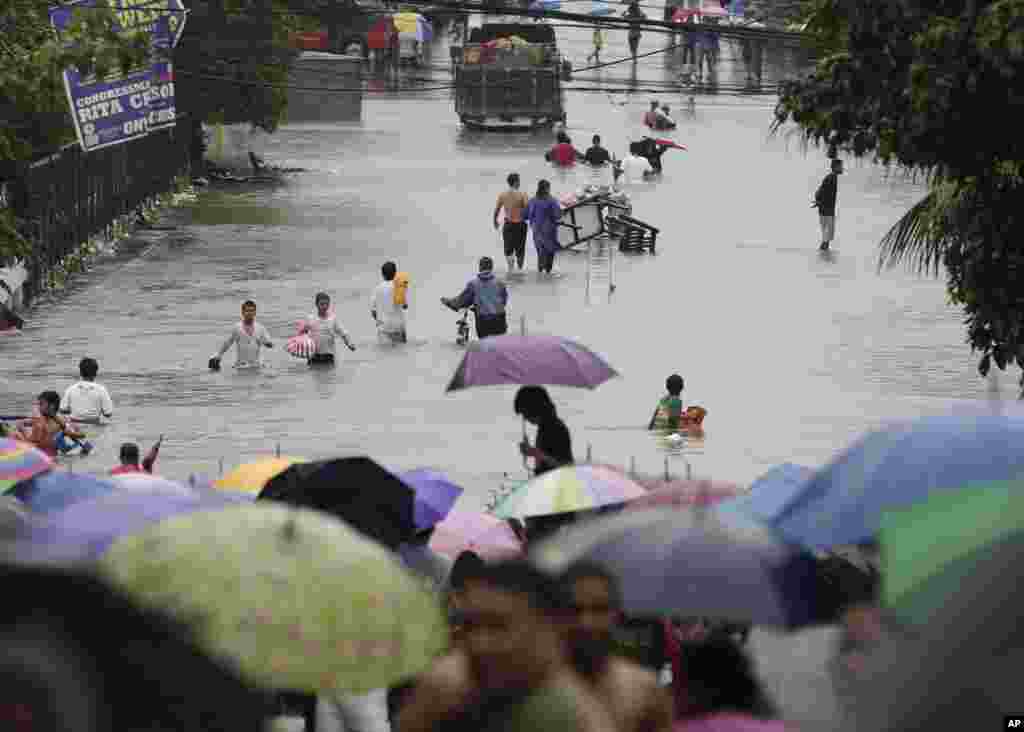 Warga harus menyeberangi banjir yang menggenangi sepanjang jalan di Quezon City, utara Manila (7/8).