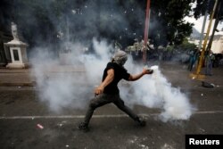 A demonstrator throws a gas canister back towards police officers during a protest against government plans to privatize health and education services, in Tegucigalpa, Honduras, April 29, 2019.