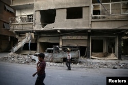 FILE - Children walk near damaged buildings in rebel-held Ain Tarma, eastern Damascus suburb of Ghouta, Syria, Sept. 17, 2016.