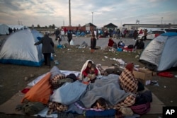 FILE - Afghan refugees are wrapped in blankets after spending the night at a collection point in the truck parking lot of the former border station on the Austrian side of the Hungarian-Austrian border.