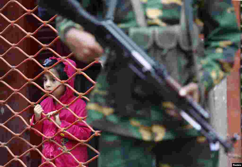 A girl watches people entering a polling booth as army soldiers stand guard during parliamentary elections in Dhaka, Jan. 5, 2014. 