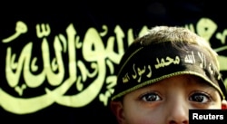 FILE - A boy stands before an Islamic jihad flag. Concern is growing in Germany and other countries that the Islamic State group, now largely weakened, has been recruiting children to carry on their jihadist legacy.