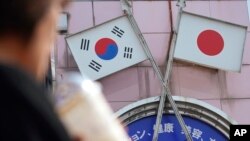 資料照：2019年8月2日，在東京新大久保地區的一家商店裡，一名女子走過印有日本國旗和韓國國旗的廣告（美聯社）。