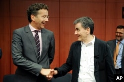 Dutch Finance Minister and chairman of the eurogroup Jeroen Dijsselbloem, left, shakes hands with Greek Finance Minister Euclid Tsakalotos during a meeting of eurozone finance ministers at the EU Council building in Brussels, Aug. 14, 2015.