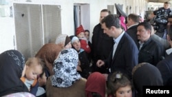 Syria's President Bashar al-Assad (C) speaks with women during his visit to displaced Syrians in the town of Adra in the Damascus countryside March 12, 2014, in this handout photograph released by Syria's national news agency SANA. 