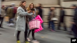 FILE - Shoppers carry their purchases as they walk along Fifth Avenue in New York, Nov. 25, 2016. 