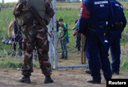 FILE - A migrant child looks at Hungarian policemen and soldier in Roszke, Hungary, Sept. 15, 2015. Hungarian police detained 16 people claiming to be Syrian and Afghan migrants for illegally crossing the Serbian border fence, a police spokeswoman said.