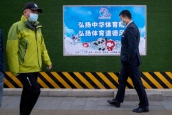 Para pejalan kaki mengenakan masker, berjalan melewati poster promosi Olimpiade Musim Dingin 2022 yang bertuliskan "Teruskan semangat olahraga China, tingkatkan sportivitas" di Beijing, Rabu, 8 Desember 2021.