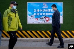 Para pejalan kaki mengenakan masker, berjalan melewati poster promosi Olimpiade Musim Dingin 2022 yang bertuliskan "Teruskan semangat olahraga China, tingkatkan sportivitas" di Beijing, Rabu, 8 Desember 2021.