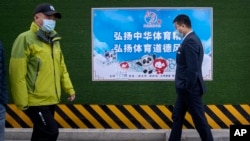 Des personnes portant des masques faciaux passent devant une affiche faisant la promotion des Jeux olympiques d'hiver de 2022 qui dit "Continuer l'esprit sportif chinois, promouvoir l'esprit sportif" à Pékin, le mercredi 8 décembre 2021.