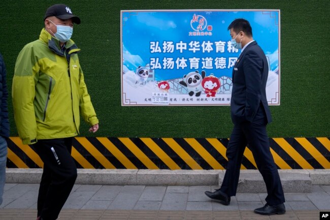 Para pejalan kaki mengenakan masker, berjalan melewati poster promosi Olimpiade Musim Dingin 2022 yang bertuliskan "Teruskan semangat olahraga China, tingkatkan sportivitas" di Beijing, Rabu, 8 Desember 2021.