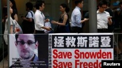 People carrying mobile phones walk past a banner supporting Edward Snowden, a former contractor at the National Security Agency (NSA), at Hong Kong's financial Central district, June 18, 2013. 